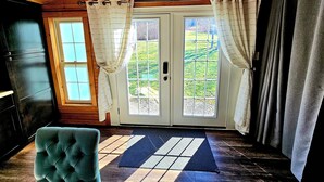 A room with a wooden ceiling, a door with glass panels, a blue rug, and a tufted chair. - The Byre Bungalow--Country Getaway, close to Yough, Fallingwater w/ Hot Tub! (Confluence)