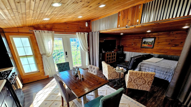 A cozy cabin interior with a wooden dining table, chairs, a sofa, and a bed. - The Byre Bungalow--Country Getaway, close to Yough, Fallingwater w/ Hot Tub! (Confluence)