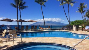 A pool area with lounge chairs and umbrellas, surrounded by palm trees and a view of a mountain. - "Sunsational" Wailea Oceanfront-WOW Views over soft sand Beach a few steps away. (Makena  Maui)