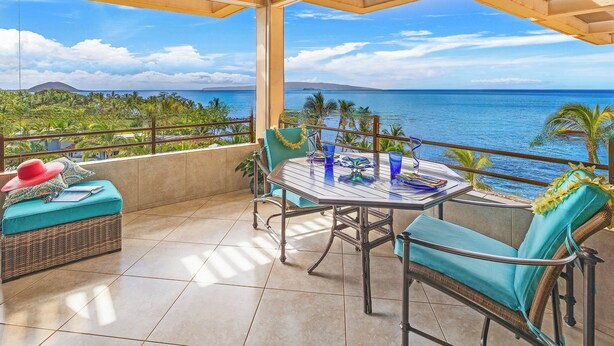 A balcony with a view of the ocean, a table with chairs, and a wicker sofa with a red hat. - "Sunsational" Wailea Oceanfront-WOW Views over soft sand Beach a few steps away. (Makena  Maui)