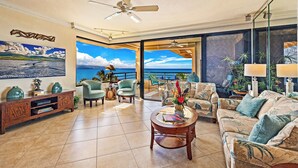 A spacious living room with a large window offering a view of the ocean, a ceiling fan, and a variety of seating including a sofa and armchairs. - "Sunsational" Wailea Oceanfront-WOW Views over soft sand Beach a few steps away. (Makena  Maui)