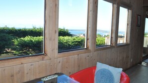 A room with large windows offering a view of greenery and a distant landscape. - Bodega Bay Gem: 180° Ocean Views, Hot Tub, Man Cave & Family Vibes – Sleeps 12 (Bodega Bay)