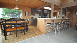 A spacious kitchen with wooden cabinets, a central island with stools, and a dining area with benches. - Bodega Bay Gem: 180° Ocean Views, Hot Tub, Man Cave & Family Vibes – Sleeps 12 (Bodega Bay)