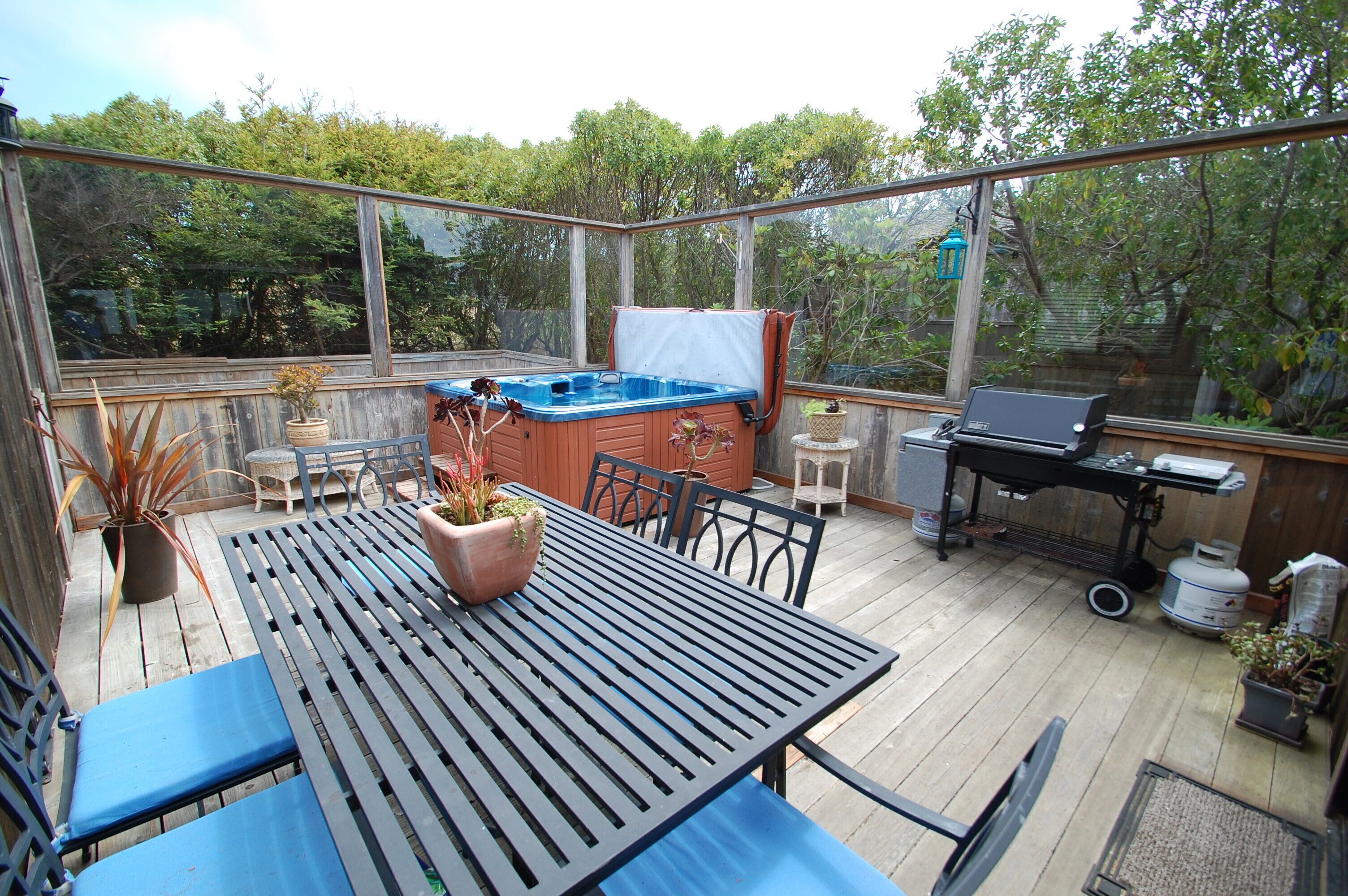 A covered patio with a hot tub, a grill, and a table with chairs.