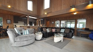 A spacious living room with a grey sofa and a black leather couch, wooden floors, and large windows. - Bodega Bay Gem: 180° Ocean Views, Hot Tub, Man Cave & Family Vibes – Sleeps 12 (Bodega Bay)
