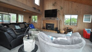 A cozy living room with a fireplace, leather sofas, and a flat-screen TV. - Bodega Bay Gem: 180° Ocean Views, Hot Tub, Man Cave & Family Vibes – Sleeps 12 (Bodega Bay)
