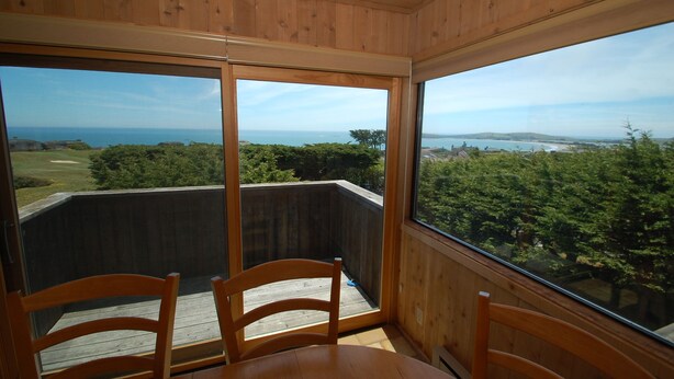 A wooden-paneled room with a view of a golf course and the sea. - Bodega Bay Gem: 180° Ocean Views, Hot Tub, Man Cave & Family Vibes – Sleeps 12 (Bodega Bay)