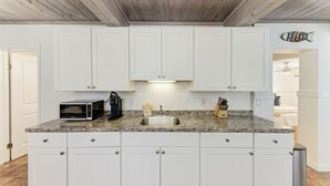 A kitchen with white cabinets, a granite countertop, a microwave, and a sink. - Pelican Perch: Tropical Paradise Cottage on the Beach            VRC17-000167 (Holmes Beach)