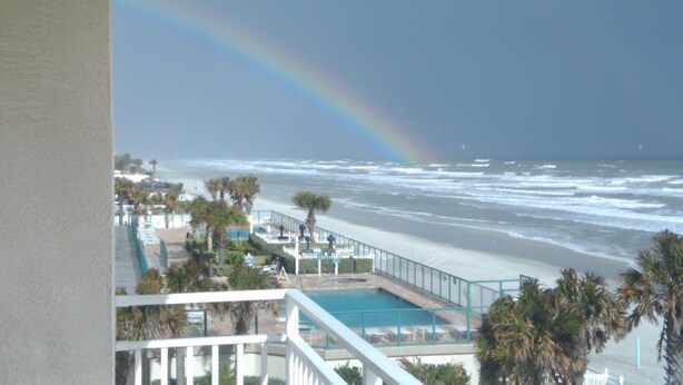 A beach view with a pool, palm trees, and a rainbow. - Dog Days of Summer on the Beach! August/Fall Dates Open
Cyndi 386-361-5882 (Daytona Beach Shores)