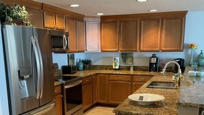 A modern kitchen with stainless steel appliances, wooden cabinets, granite countertops, and a stainless steel trash can. - Dog Days of Summer on the Beach! August/Fall Dates Open
Cyndi 386-361-5882 (Daytona Beach Shores)