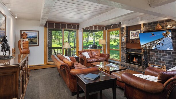 A cozy living room with leather sofas, a fireplace, and a large TV screen. - Top of the Village~Ski-in/out~HT~Pool~Grill~Parking (Snowmass Village)