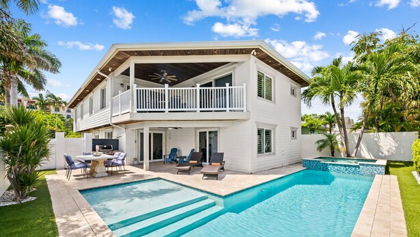 Ein zweistöckiges Haus mit Swimmingpool, Sitzgelegenheiten im Freien und einem Balkon.