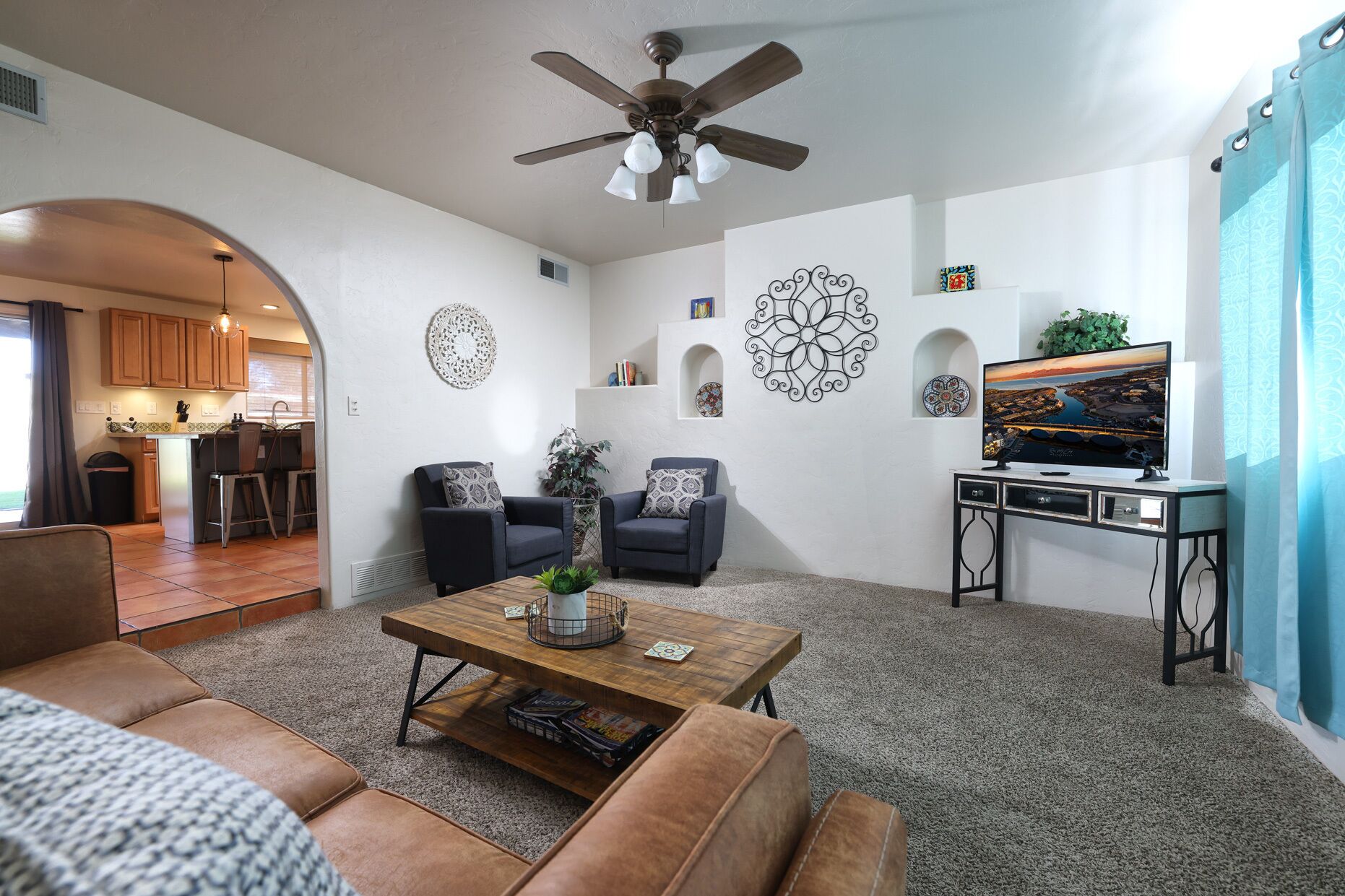 A living room with a coffee table, sofas, a TV, decorative wall art, and a ceiling fan.