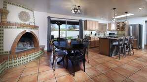 A spacious kitchen with a central island, a built-in brick oven, and a dining area with a round table and chairs. - Luxe Desert Escape: 15Min to Downtown ~ Pool ~ Spa ~ BBQ ~ Amazing desert views! (Tucson)
