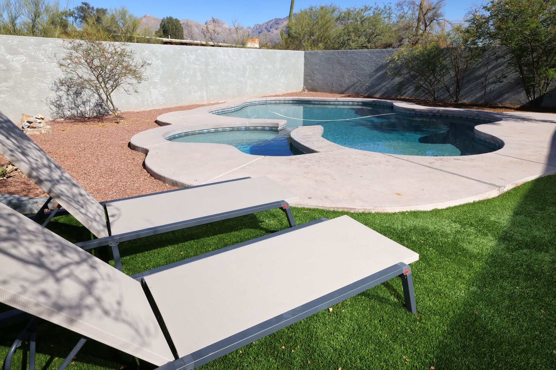 Un patio trasero con piscina, césped y un muro de concreto.