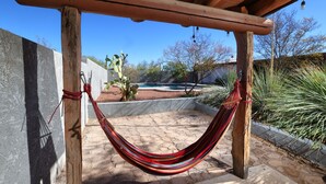 A hammock suspended between wooden posts in a covered outdoor area with a pool and desert plants in the background. - Luxe Desert Escape: 15Min to Downtown ~ Pool ~ Spa ~ BBQ ~ Amazing desert views! (Tucson)