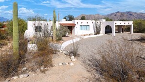 A desert-style building with a white exterior, arched entryway, and a view of mountains in the background. - Luxe Desert Escape: 15Min to Downtown ~ Pool ~ Spa ~ BBQ ~ Amazing desert views! (Tucson)