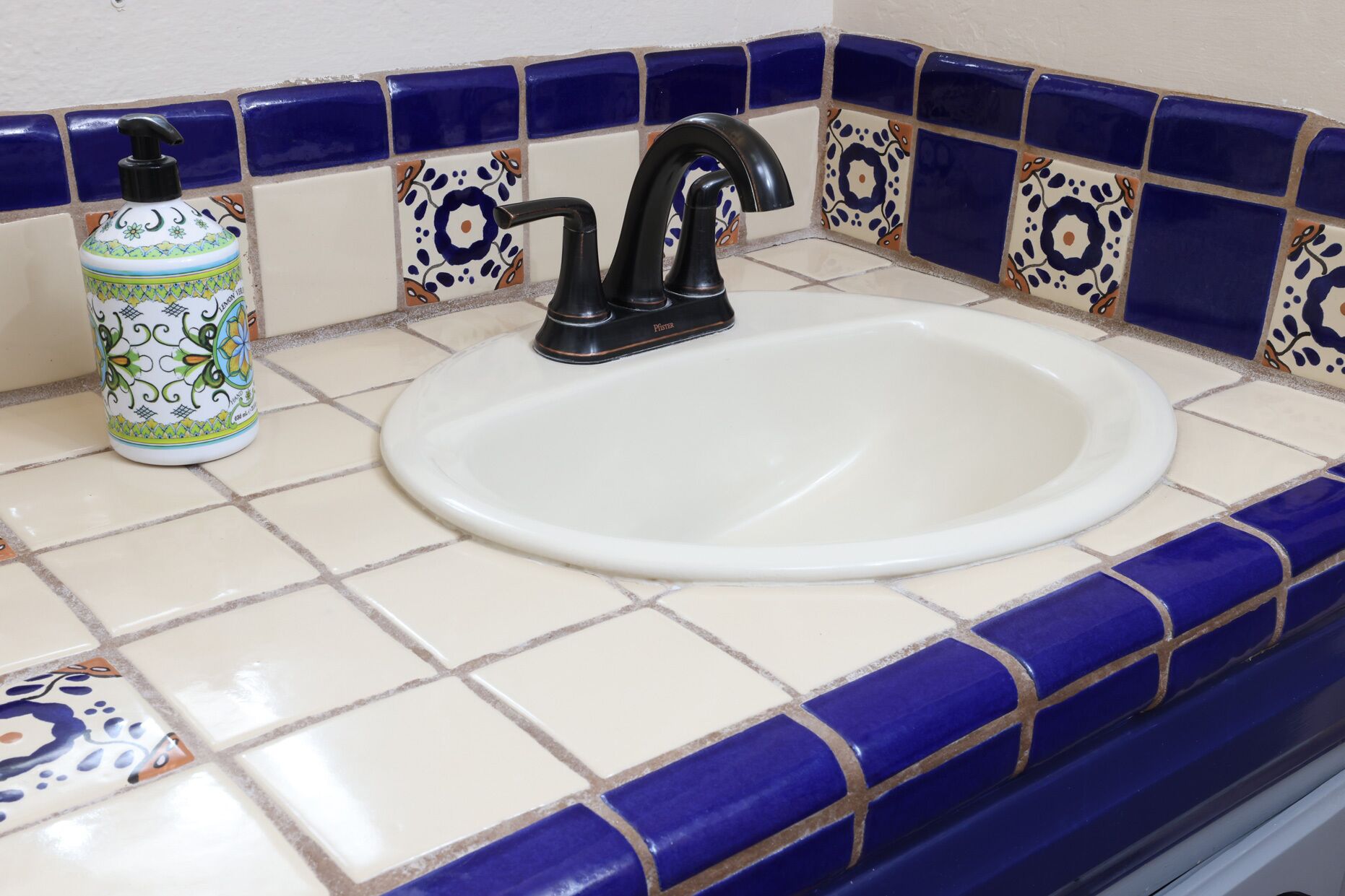 Uma pia de banheiro com uma torneira preta e um dispensador de sabão em uma bancada azulejada.