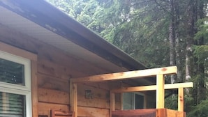 A wooden cabin with a door open, revealing a window and a small outdoor area with gravel and stepping stones.