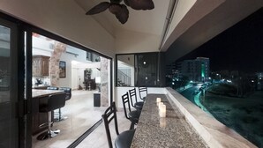 Une cuisine moderne avec un mur en pierre, un coin repas avec un bar et un balcon offrant une vue sur le paysage urbain la nuit.