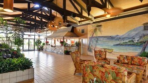 Eine geräumige Lobby mit hoher Decke, Holzbalken und einem Wandbild von einem tropischen Strand.