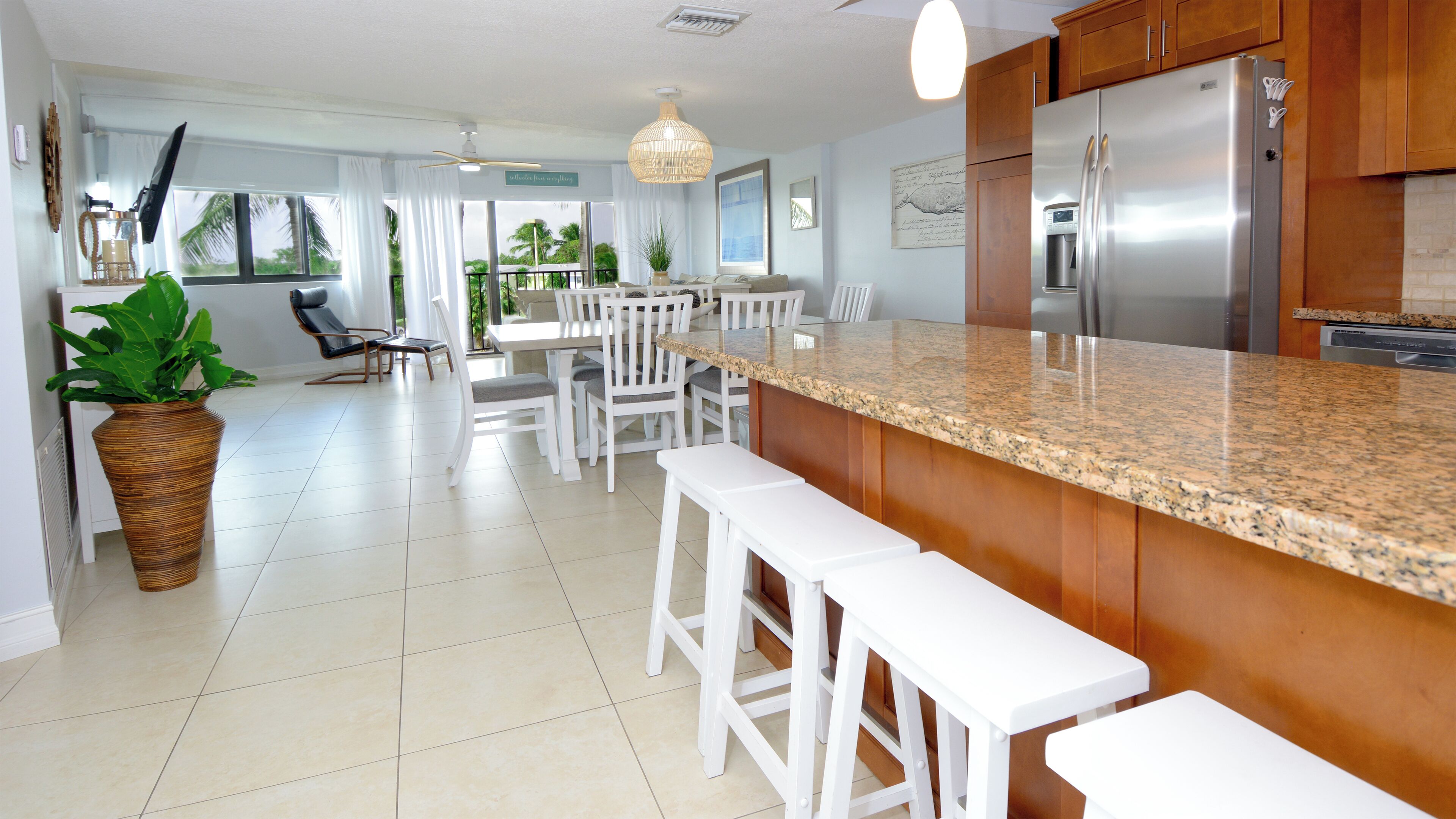 A modern kitchen with a granite countertop, white bar stools, and a stainless steel refrigerator.