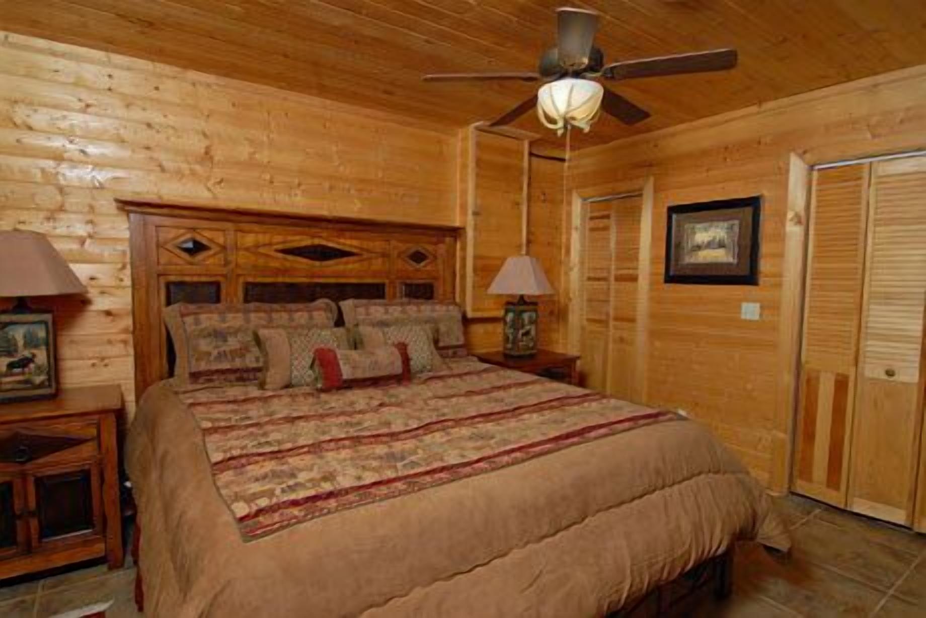 A log cabin bedroom with a bed, a ceiling fan, a nightstand, and a framed picture on the wall.