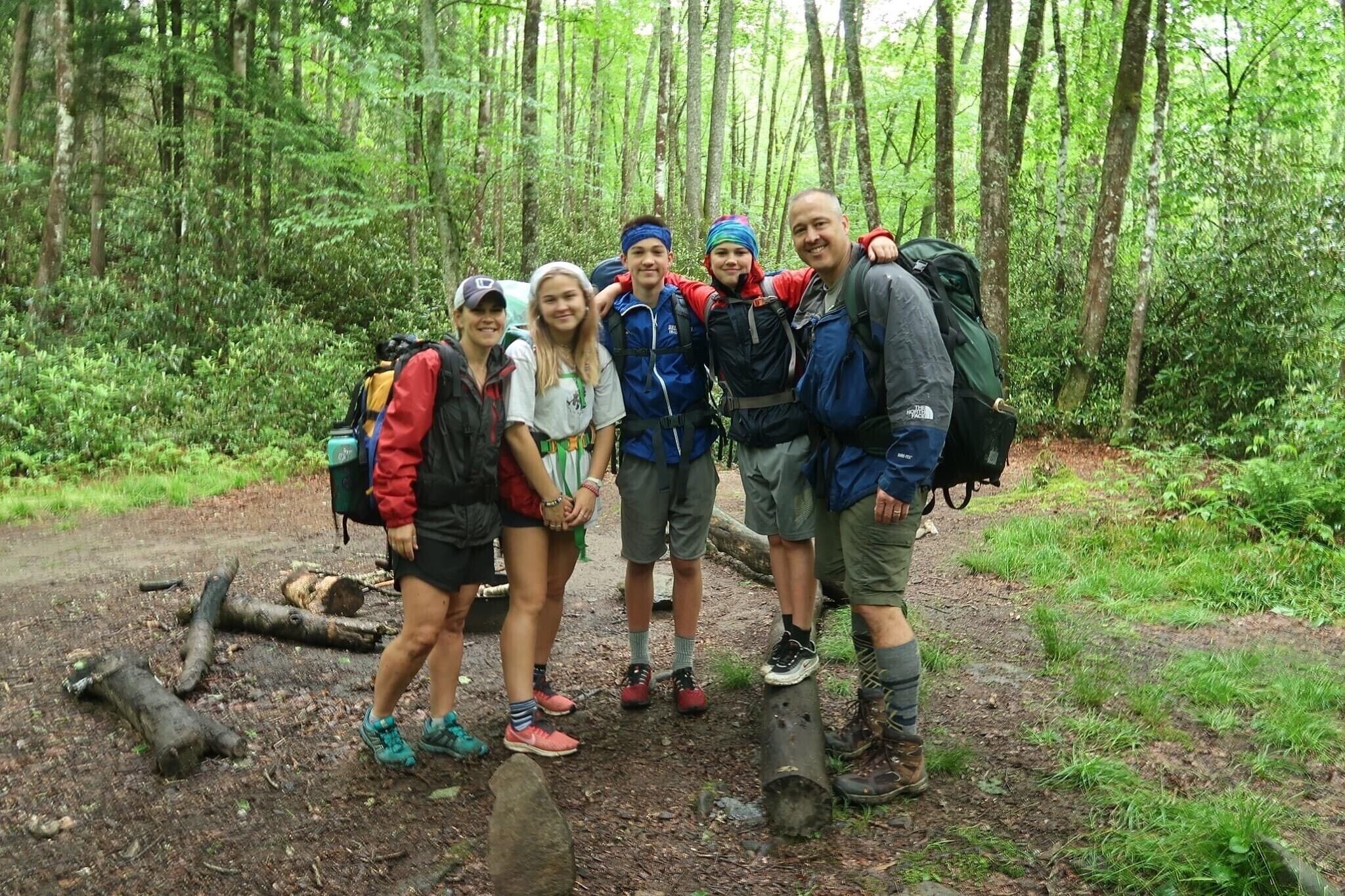A group of people in a forested area with backpacks, suggesting a hiking or outdoor activity.