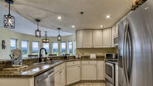 A modern kitchen with granite countertops, stainless steel appliances, and large windows offering a view of the outdoors.