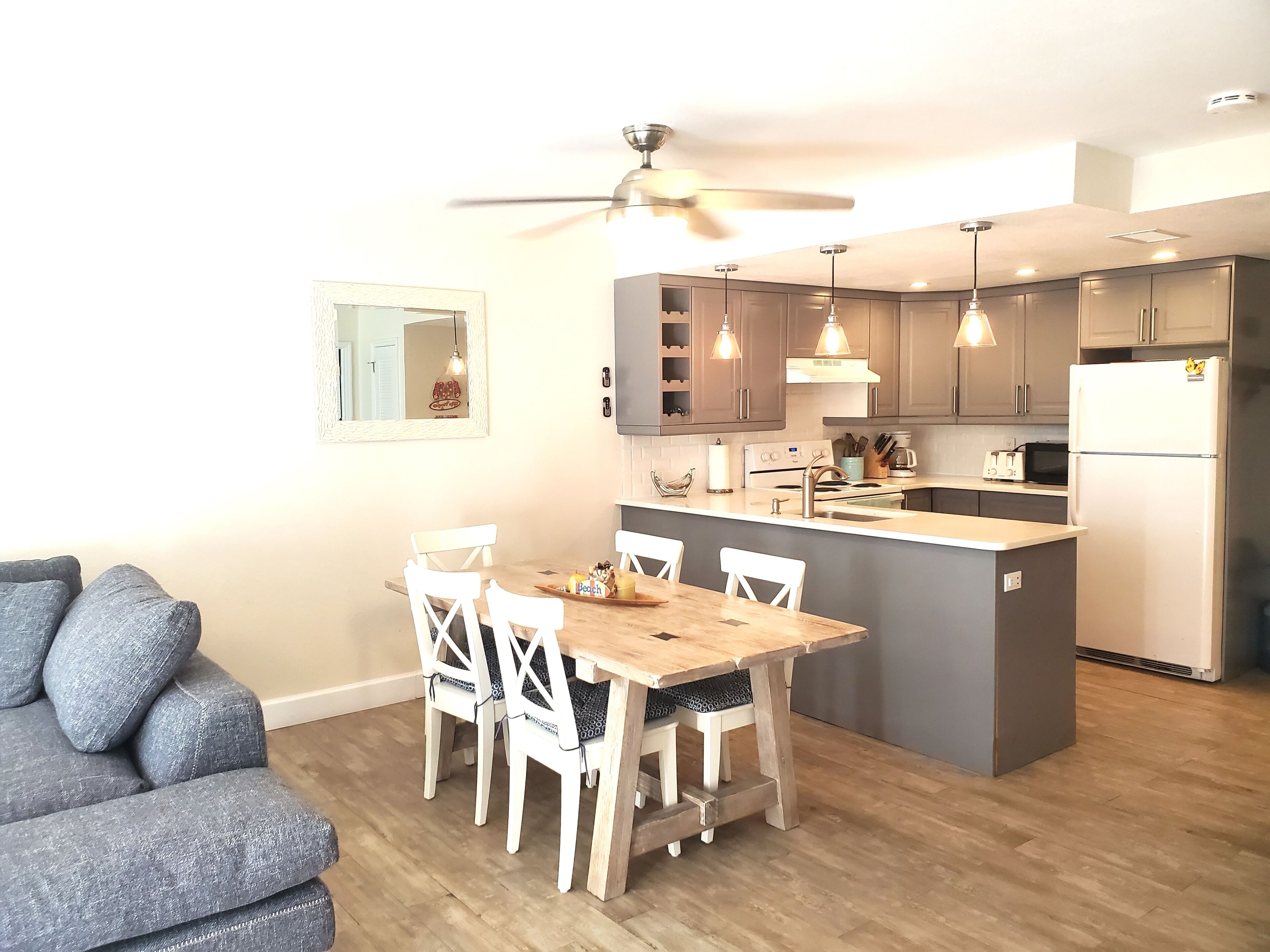 Una cocina moderna con una isla central, mesa de comedor de madera y sillas blancas.