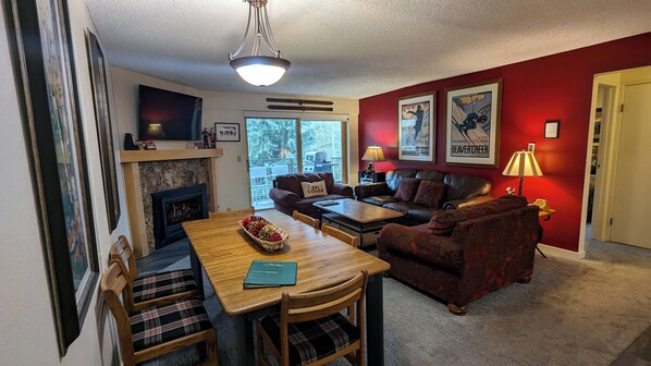 A cozy living room with a fireplace, a dining table with chairs, a sofa, and a red accent wall.