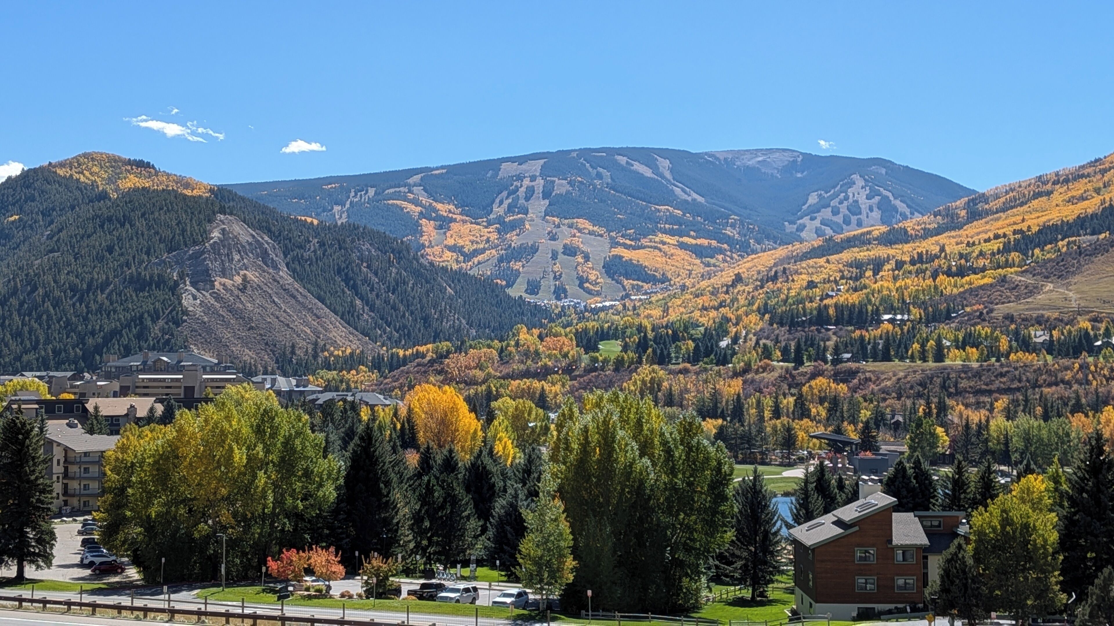 Paisagem montanhosa com folhagem outonal, uma estrada e edifícios em primeiro plano.