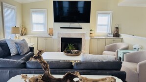 A living room with a fireplace, a large flat-screen TV, and a modern coffee table. -  Make Memories at Barefoot Daze (Kitty Hawk)