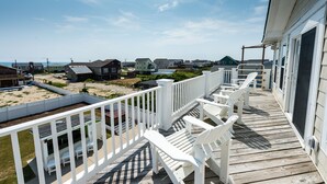 A wooden deck with white railings and chairs, overlooking a beach and houses. -  Make Memories at Barefoot Daze (Kitty Hawk)