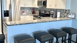 A modern kitchen with white cabinets, stainless steel appliances, a granite countertop, and a bar area with stools.