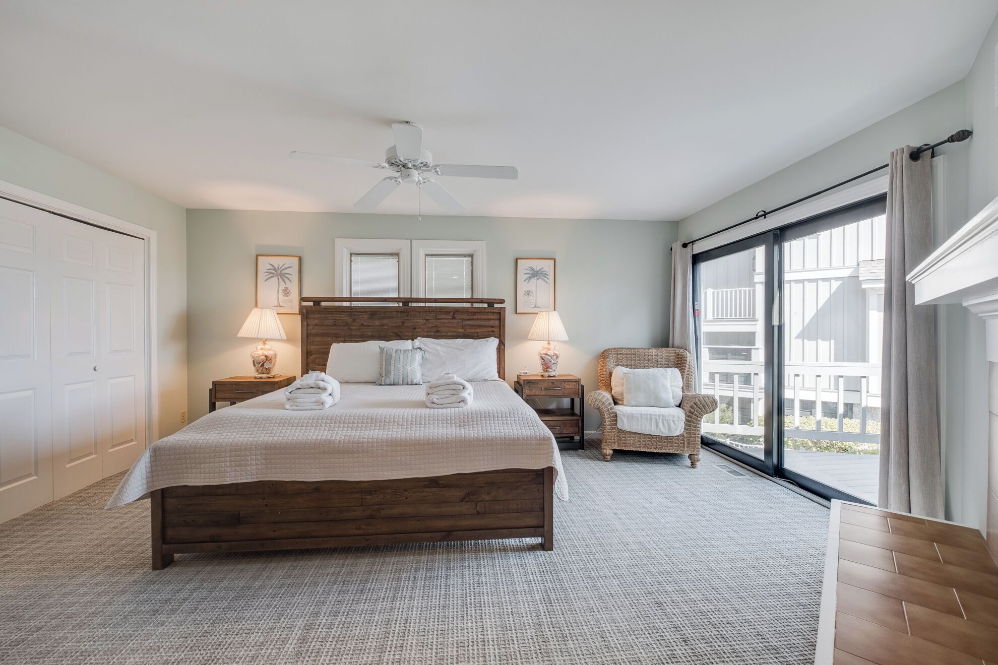 A bedroom with a large bed, two bedside tables with lamps, a chair, and a ceiling fan.