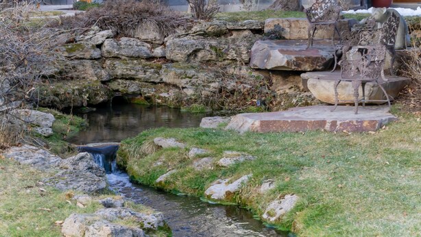 Un petit ruisseau serpente à travers un jardin rocheux, agrémenté de marches en pierre et de bancs en métal.