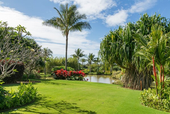 A lush garden with a pond, palm trees, and red flowers.