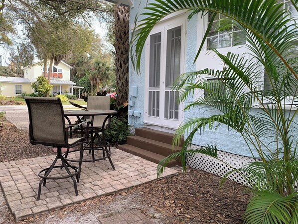 A patio with a table and chairs, a white door, and a small garden area with a palm tree.