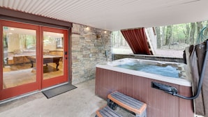 A hot tub area with a stone wall, wooden deck, and a glass door leading to an indoor space. - “Mountain Escape-7BR, Game Room, Fire Pit Close to Skiing and Trails!” (Lake Harmony)
