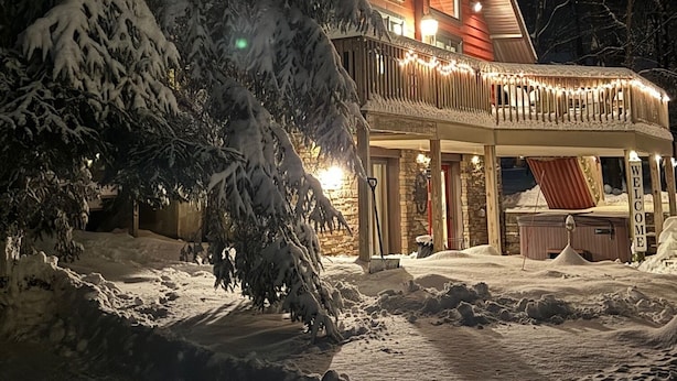A large, modern log cabin with a wrap-around porch, surrounded by snow-covered trees. - “Mountain Escape-7BR, Game Room, Fire Pit Close to Skiing and Trails!” (Lake Harmony)