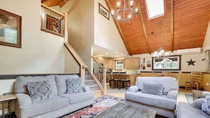 A spacious living area with a high ceiling, wooden beams, and a staircase leading to an upper level. - “Mountain Escape-7BR, Game Room, Fire Pit Close to Skiing and Trails!” (Lake Harmony)