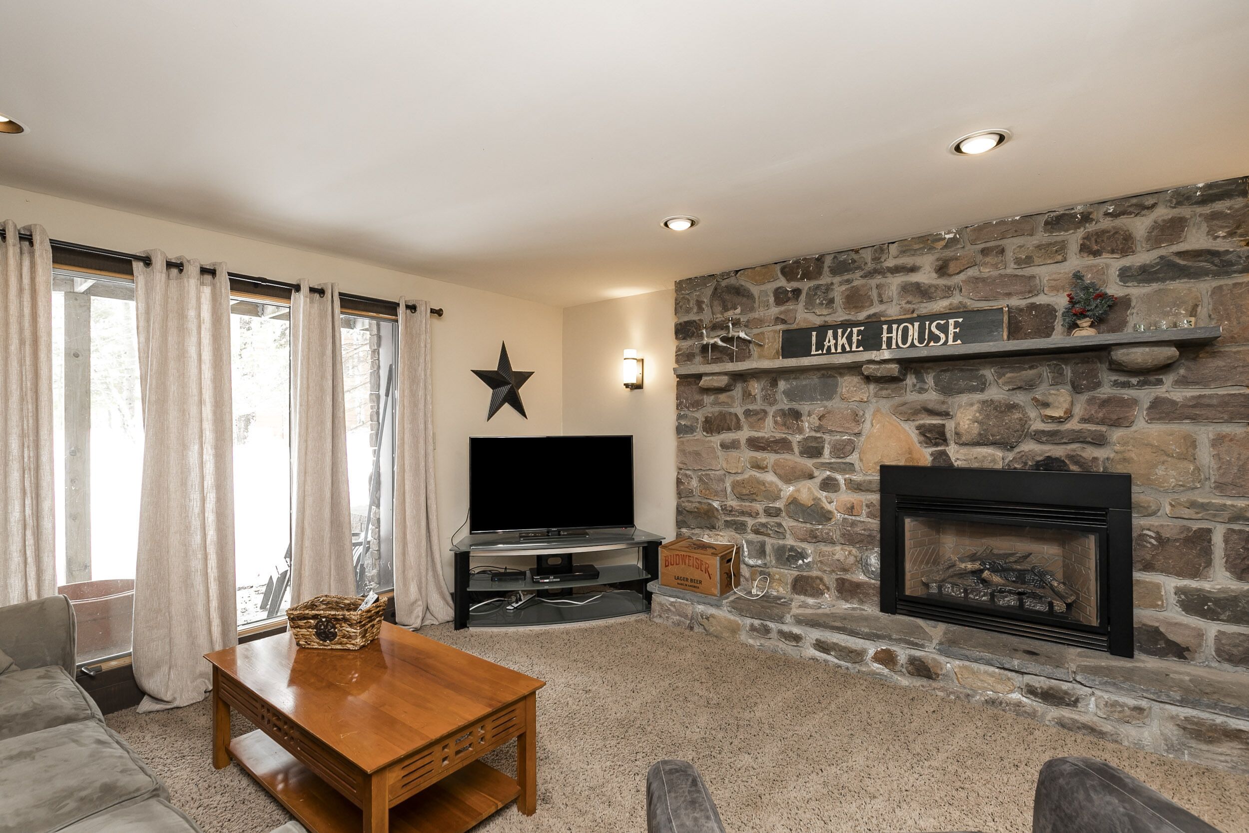 A living room with a stone fireplace, a television, and a sign that reads "LAKE HOUSE".