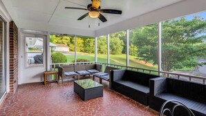 Un patio couvert avec un ventilateur de plafond, des sièges d’extérieur et une vue sur un terrain de golf.