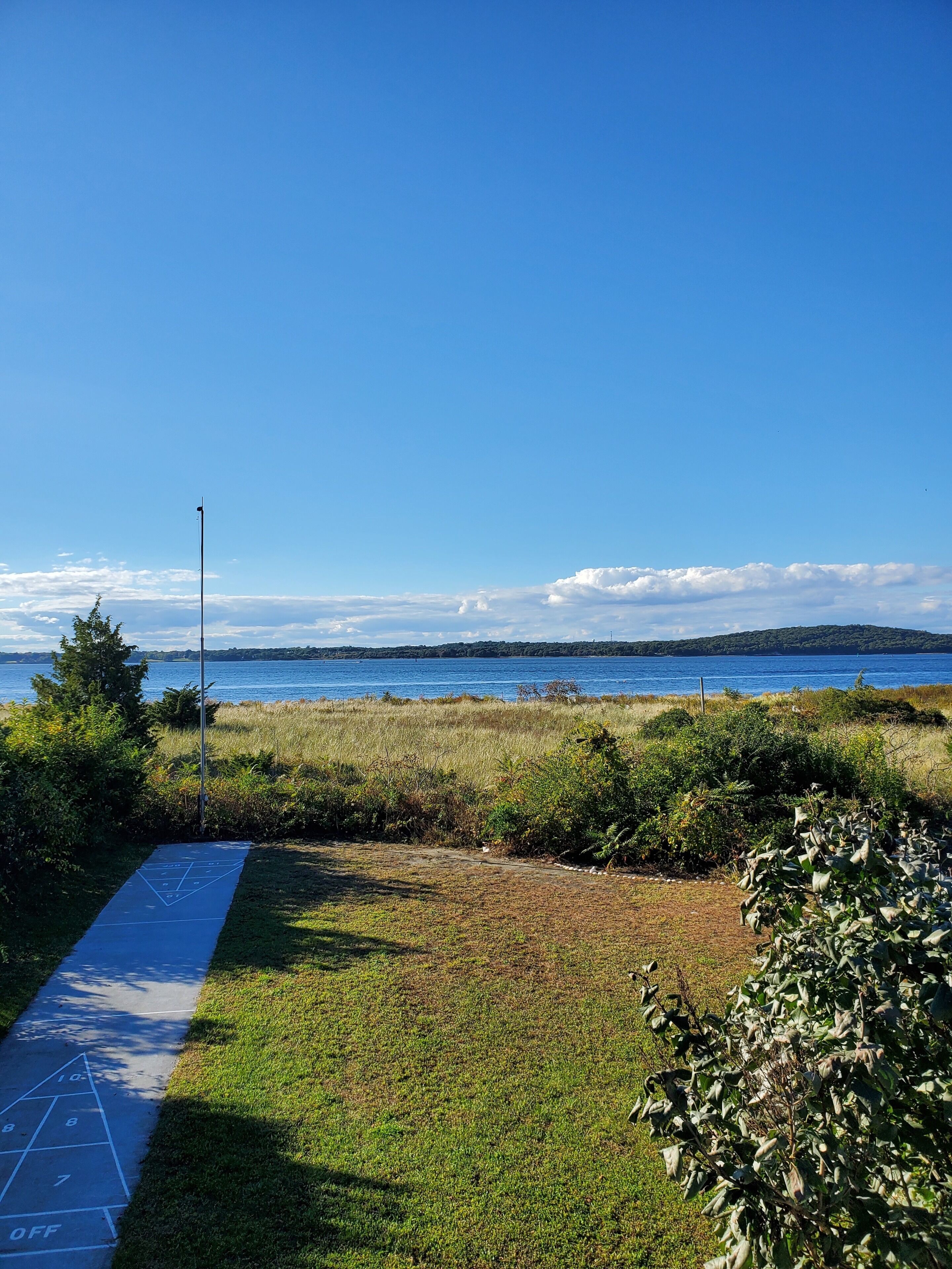 On aperçoit clairement un lac, avec une rive éloignée, une zone herbeuse où l’on joue à la marelle, et un poteau en métal.