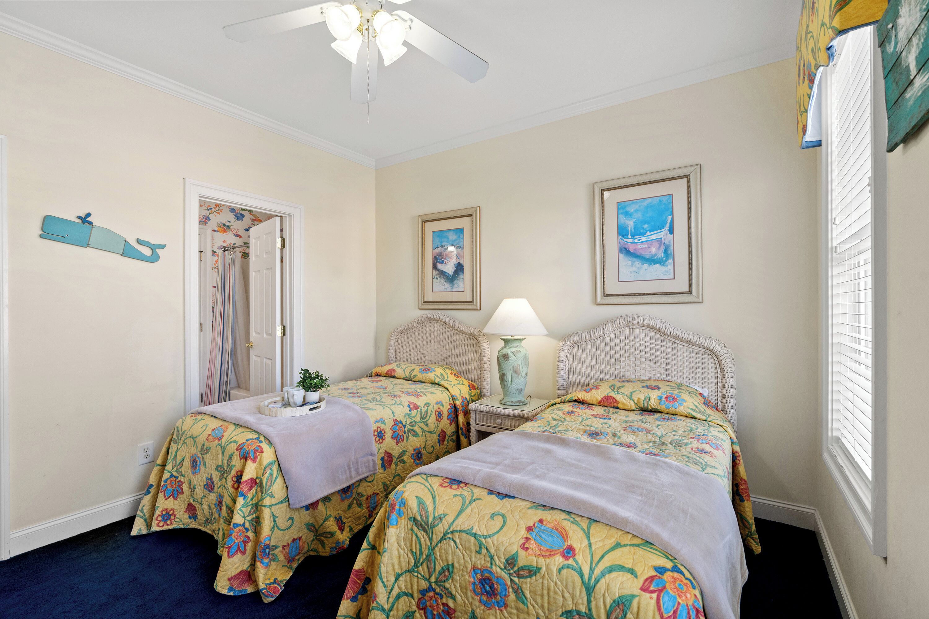 Une chambre avec deux lits, un ventilateur de plafond, une fenêtre avec des stores et une porte donnant sur une salle de bain.