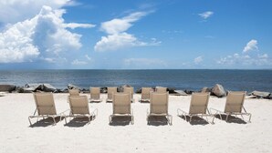 Une plage bordée de rangées de chaises longues beiges, toutes orientées vers l’océan.