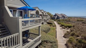 Une propriété située en bord de mer, dotée de plusieurs balcons, d’une terrasse en bois et offrant une vue dégagée sur l’océan.