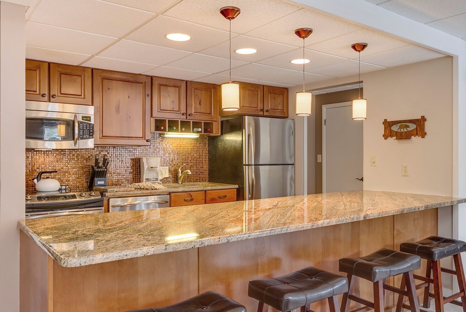 A kitchen with wooden cabinets, stainless steel appliances, a granite countertop, and bar stools.
