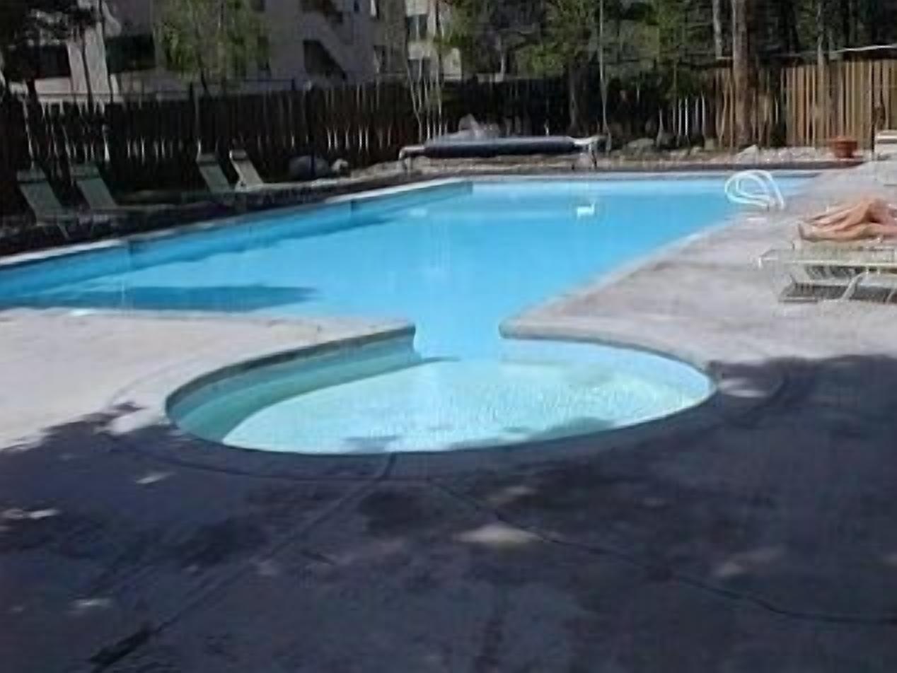 Une piscine avec un jacuzzi circulaire au centre, entourée de chaises longues et d’une clôture en bois.
